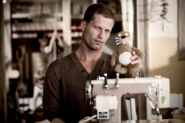 A man with a plush toy, next to a sewing machine