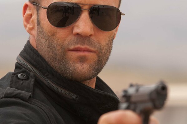 Jason Statham à lunettes avec un pistolet