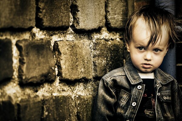 A little boy stands against a brick wall