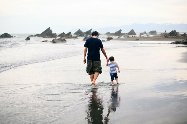 Ein Mann mit seinem Sohn mit dem Rücken am Meer spazieren gehen