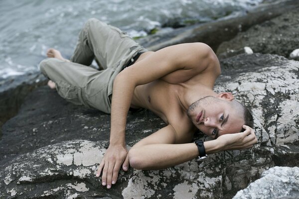 A man poses on a rock by the water