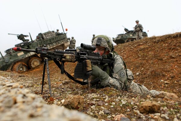 Un soldat vise sur fond de véhicules blindés de transport de troupes