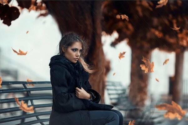 Autumn a beautiful girl is sitting on a bench