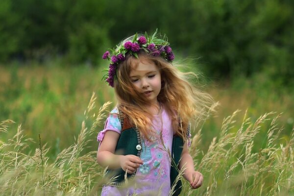 La niña de la corona corre por el campo. Paisaje de verano