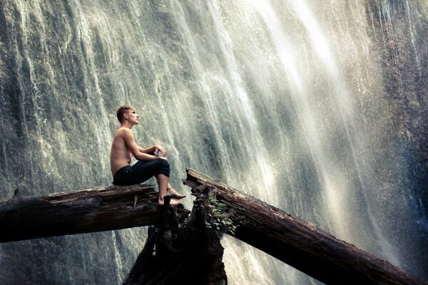 Ragazzo seduto su un albero vicino a una cascata