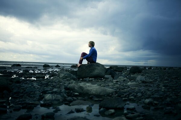 Ragazzo seduto sulle rocce e guardando il mare