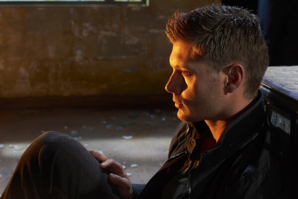 Dean Winchester is sitting on the floor with a mournful face