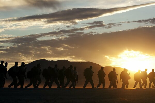 Żołnierze na tle góry idą ku zachodowi słońca