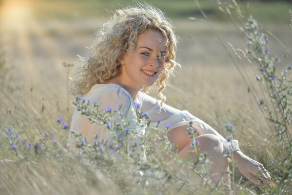 Curly blonde with a smile is sitting in a field