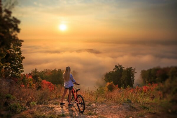 Fille avec un vélo en regardant le coucher de soleil sur une falaise