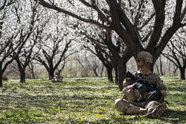 Żołnierz siedzi z bronią w ogrodzie