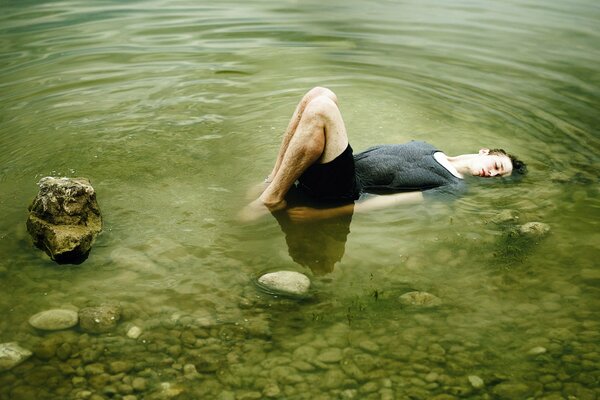 The guy is lying on the rocks in a lake with green water