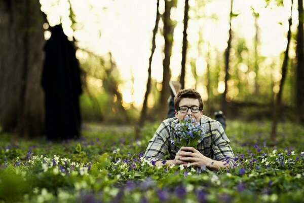 The guy is lying on the grass with a bouquet of flowers