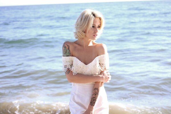 Blondine mit Tattoos auf dem Hintergrund der Wellen