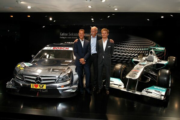 Schumacher und zwei Männer stehen neben zwei Autos