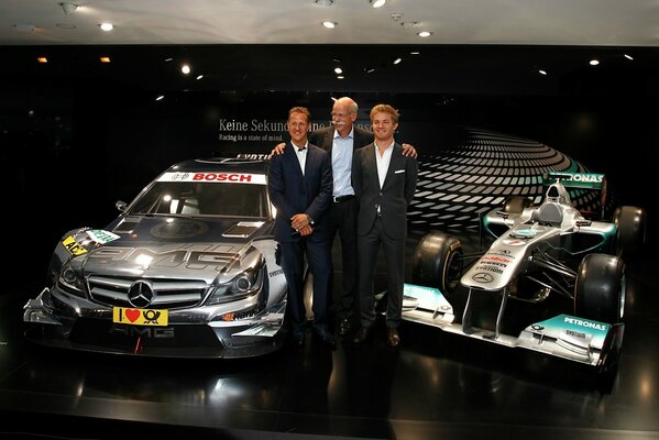 Schumacher and two men are standing next to two cars