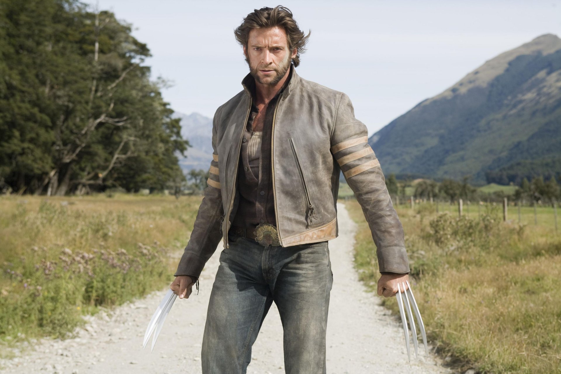 hugh jackman wolverine james logan guapo actor hombre héroe mutante x-men cuchillos garras punta vista arena polvo chaqueta montañas árboles cielo