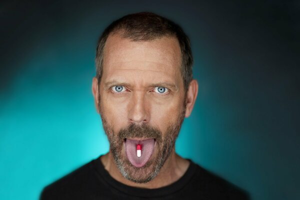 Hugh Laurie avec une pilule sur la langue