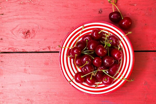 Cherry in a striped plate on a background of boards