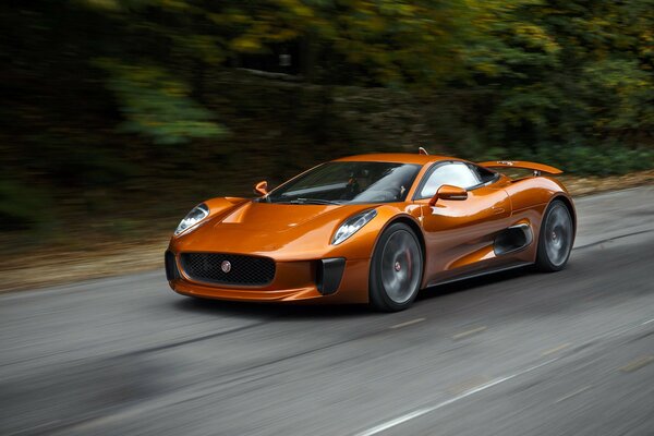 Оранжевый Jaguar spectre быстро едет по дороге