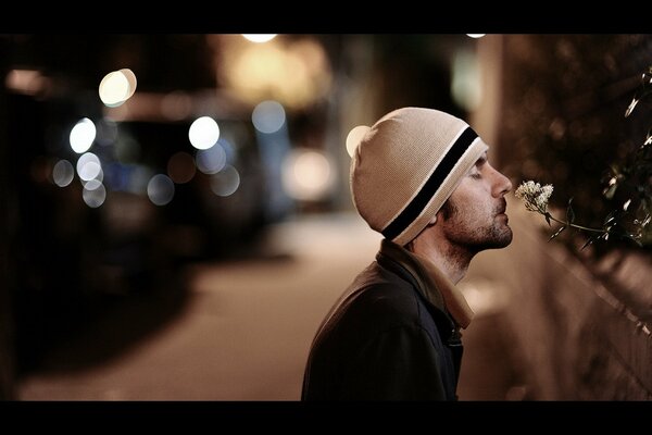 A man on the street sniffs a flower