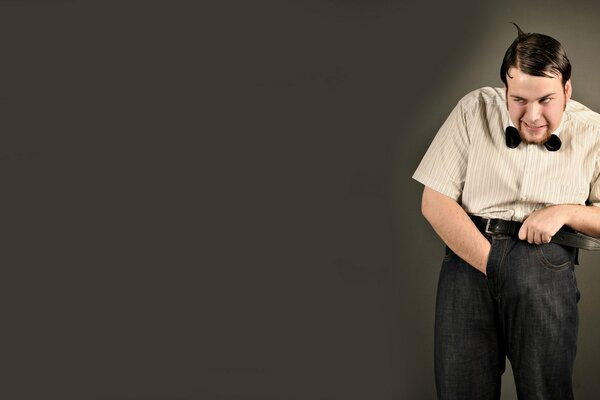 A nerd on a gray background holds a belt with one hand, his other hand is in jeans