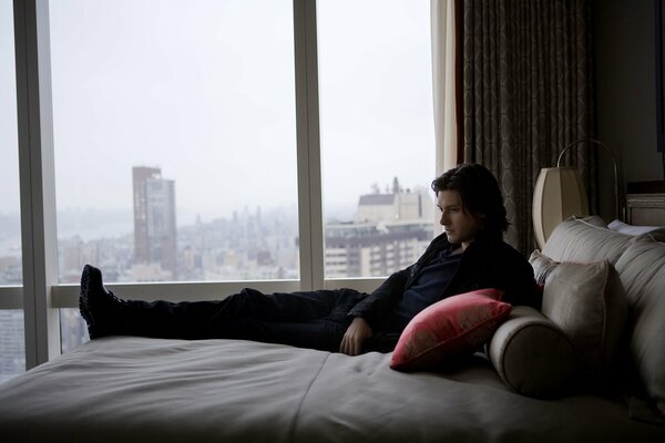 Tapete mit Ben Barnes auf einem Bett mit Kissen. Stadt vor dem Fenster