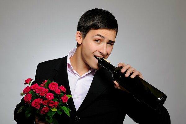 Netter junger Mann mit einem Blumenstrauß in der Hand trinkt Wein aus einer Flasche