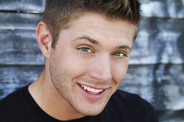 A smiling actor in a black supernatural T-shirt