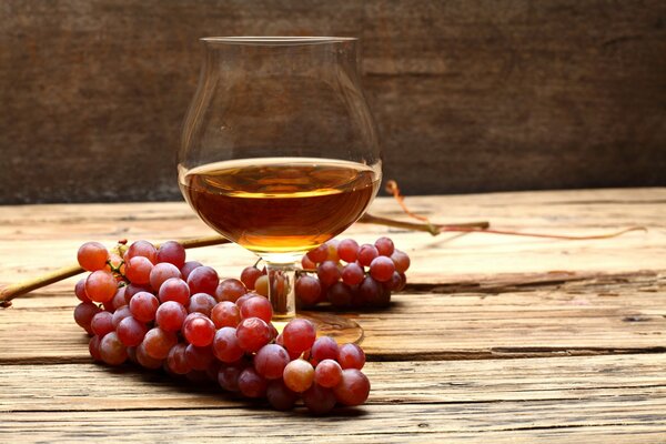A glass of cognac and a bunch of grapes on the table
