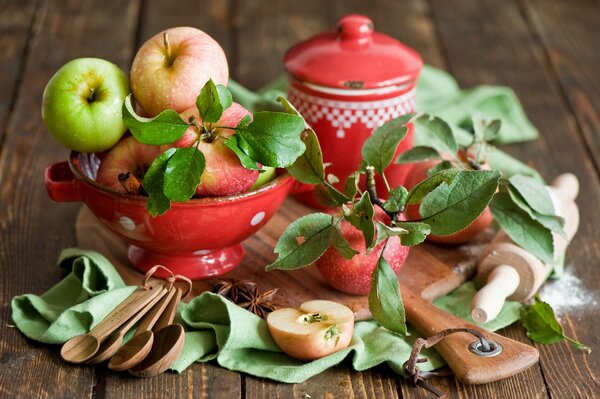 En un tablero de madera, fruta en un frutero, rodillo, sartén, cucharas de Madera y manzanas con hojas