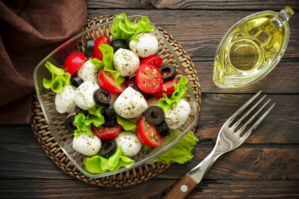 Natura morta con insalata caprese brillante, forchetta e olio d oliva per condire