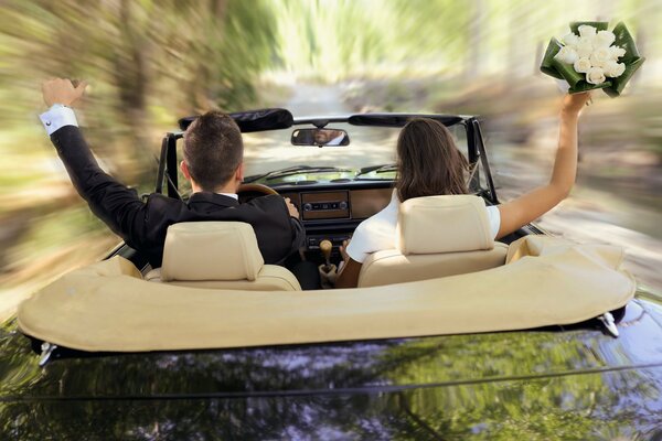 Un chico con un traje y una chica con un ramo corren en un convertible