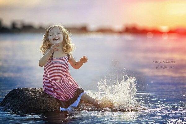 Una niña chapoteando en la orilla. Puesta de sol en el agua