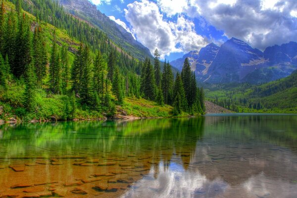 A clear mountain lake with a rocky bottom reflects clouds