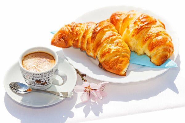 A cup of coffee on a saucer with a spoon and croissants on a plate