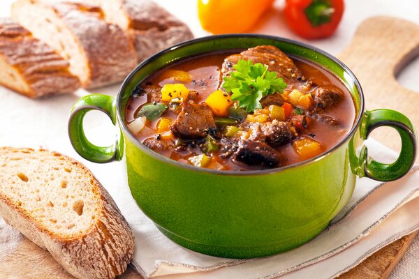 Suppe mit Fleisch in einem grünen Topf, frisches Brot