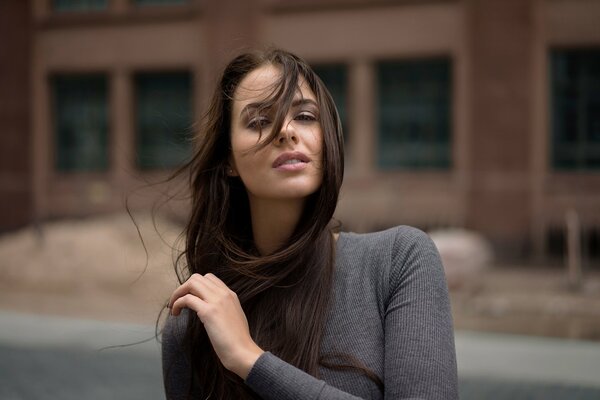 A girl poses in the wind against the background of a building