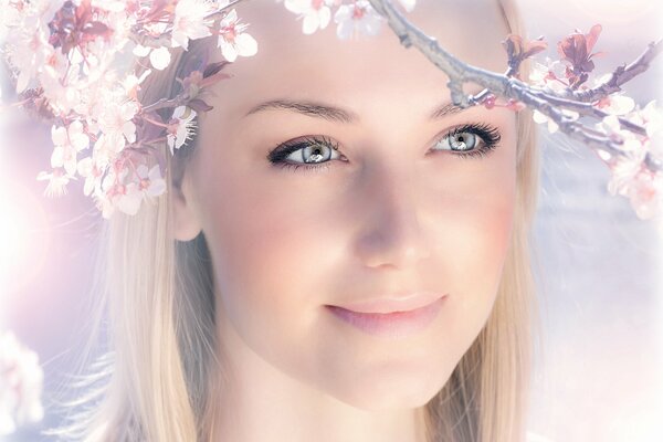 Das Gesicht des Mädchens mit einem Lächeln auf dem Hintergrund der Frühlingsblüte