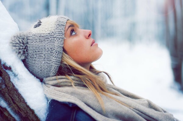 Ritratto invernale di una bionda in un cappello su uno sfondo di neve