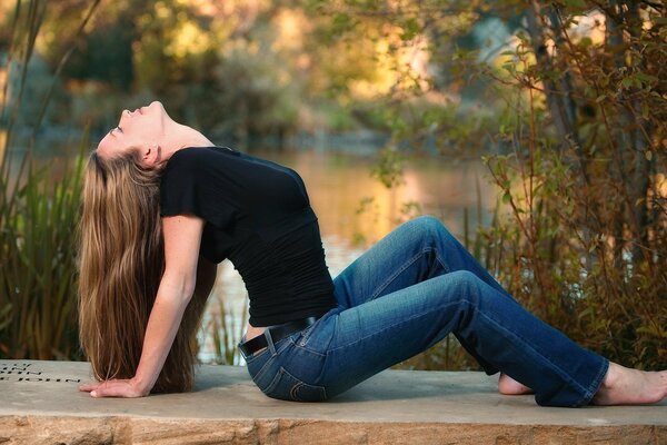 Chica en jeans junto al lago con cintura delgada