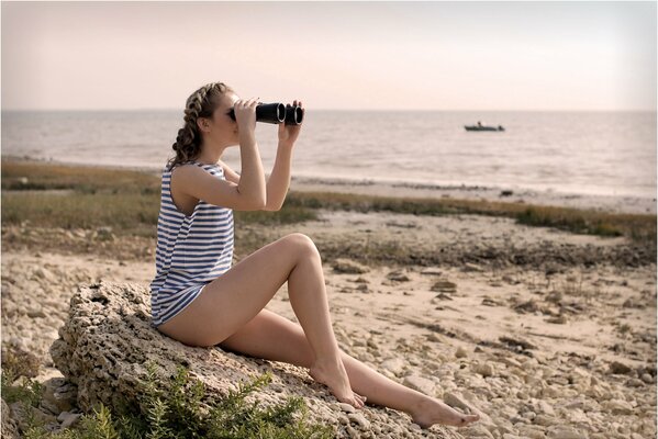 A girl in a vest on the shore looks through binoculars