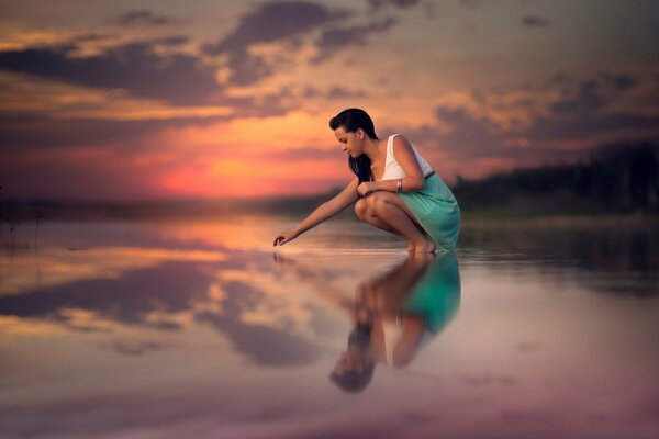 A girl touches the surface of the lake water at sunset