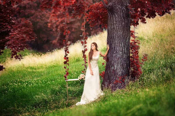 A girl stands next to a swing and a tree