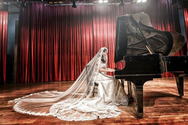 Chica asiática en vestido de novia y velo toca el piano