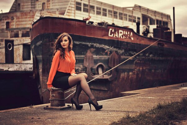 Красивая девушка сидит на фоне корабля