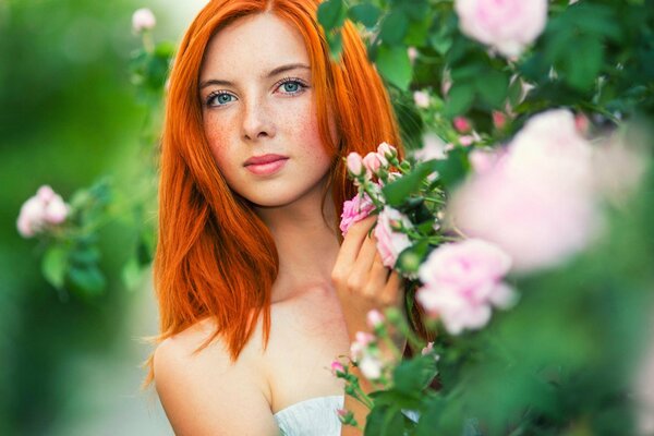 Portrait of a red-haired girl with freckles in flowers