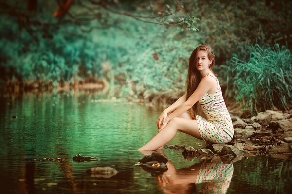 Jeune fille assise dans la forêt sur les rochers à côté de la rivière