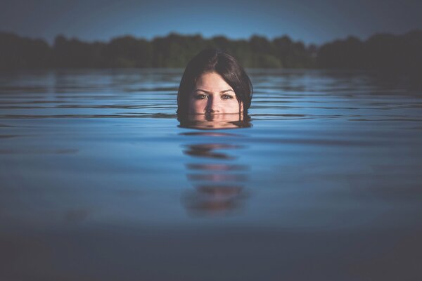 A girl with dark hair swims in a lake