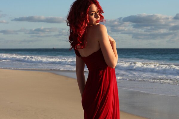 Chica con el pelo rojo y vestido rojo de pie en el fondo de las olas